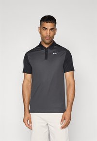 Pelēks polo krekls ar melnu apkakli un īsām piedurknēm, ar baltu Nike logo kreisajā krūtī un pogu aizdari.