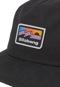 Sort kasket lavet af stof, med en rektangulær logo-patch med bølger og solnedgangsfarver i orange, lilla og blå.
