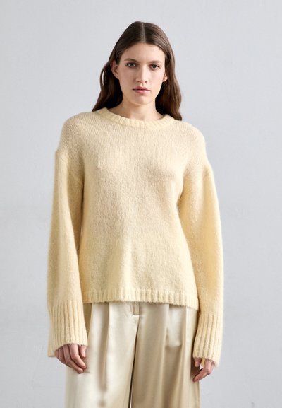 Πλεκτή μπλούζα σε μαλακό, ανοιχτό κίτρινο χρώμα με στρογγυλή λαιμόκοψη, φαρδιά μανίκια και ριχτό τελείωμα. Συνδυάζεται με ανοιχτόχρωμες πτυχωτές παντελόνες.