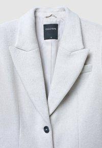 Cappotto grigio chiaro in misto lana con rever a lancia, chiusura con un solo bottone e un'etichetta con la scritta "CALLIOPE" nella taglia piccola. La fodera interna è liscia.