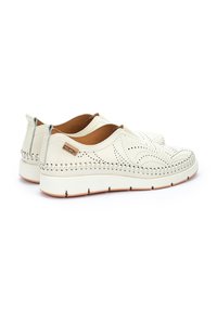 Zapatillas blancas sin cordones, hechas de cuero perforado, con un acento de costura texturizada alrededor de la suela y un forro interior marrón.