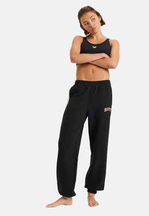 Svarta sweatpants med dragsko i midjan och Roxy-logotyp i rosa. Matchat med en svart croptop. Sidenmjuk tyg, avslappnad passform.