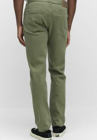 Olivgrön byxor med rak passform, med bakfickor och en brun läderpatch vid midjan. Bärs med svarta sneakers.