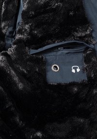 Tissu en fausse fourrure noire avec une poche zippée bleu marine dotée d'un œillet en métal et d'un symbole de casque blanc.