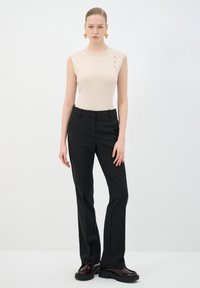 Top sin mangas beige con tres botones dorados en el hombro, combinado con pantalones negros a medida y zapatos de plataforma burdeos.