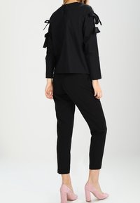 Svart blus med långa ärmar och rosettaccenter på axlarna, kombinerad med skräddarsydda svarta byxor och ljusrosa högklackade skor.