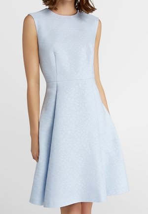 Ärmelloses, hellblaues, floral strukturiertes A-Linien-Kleid mit tailliertem Oberteil und ausgestelltem Rock, getragen von einer Frau mit kurzen Haaren.