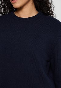 Marineblauer gestrickter Pullover mit Rundhalsausschnitt, gerippter Textur und lockerer Passform. Der Stoff wirkt weich und bequem, ohne sichtbare Muster.