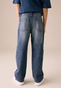 Plave traperice širokog kroja s visokim strukom, dva stražnja džepa i izblijedjeli izgled. Kombinirane s bijelim tenisicama.