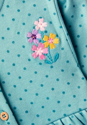 Helles blaues Material mit dunkelblauen Punkten. Mit floralem Stickereien in Pink, Lila und Gelb; Holzknopf-Akzent in der Nähe der Knopfleiste.