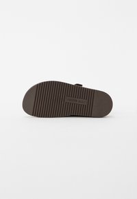 Sole of a dark brown sandal with ridged tread pattern and "Steve Madden" logo embossed in the center.