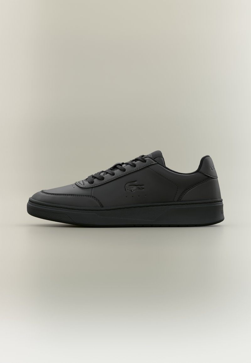 Baskets basses noires avec fermeture à lacets, dessus en cuir lisse et logo crocodile embossé sur le côté.