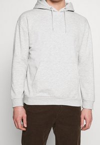 Sudadera de algodón gris claro con un bolsillo frontal, capucha con cordón y puños acanalados, que presenta una textura suave y un diseño casual.