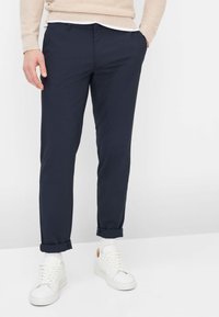 Pantaloni blu navy affusolati con finitura in tessuto liscio. Orli arrotolati e chiusura frontale con bottoni. Abbinati a sneaker bianche e calzini alla caviglia.