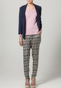 Blazer azul marino sobre una blusa rosa con escote en V, combinado con pantalones de patrón blanco y negro y sandalias de plataforma beige. Texturas suaves y ajuste entallado.