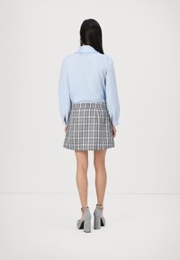 Light blue blouse with ruffled collar, paired with a grey plaid mini skirt. The outfit is completed with gray block-heeled shoes.