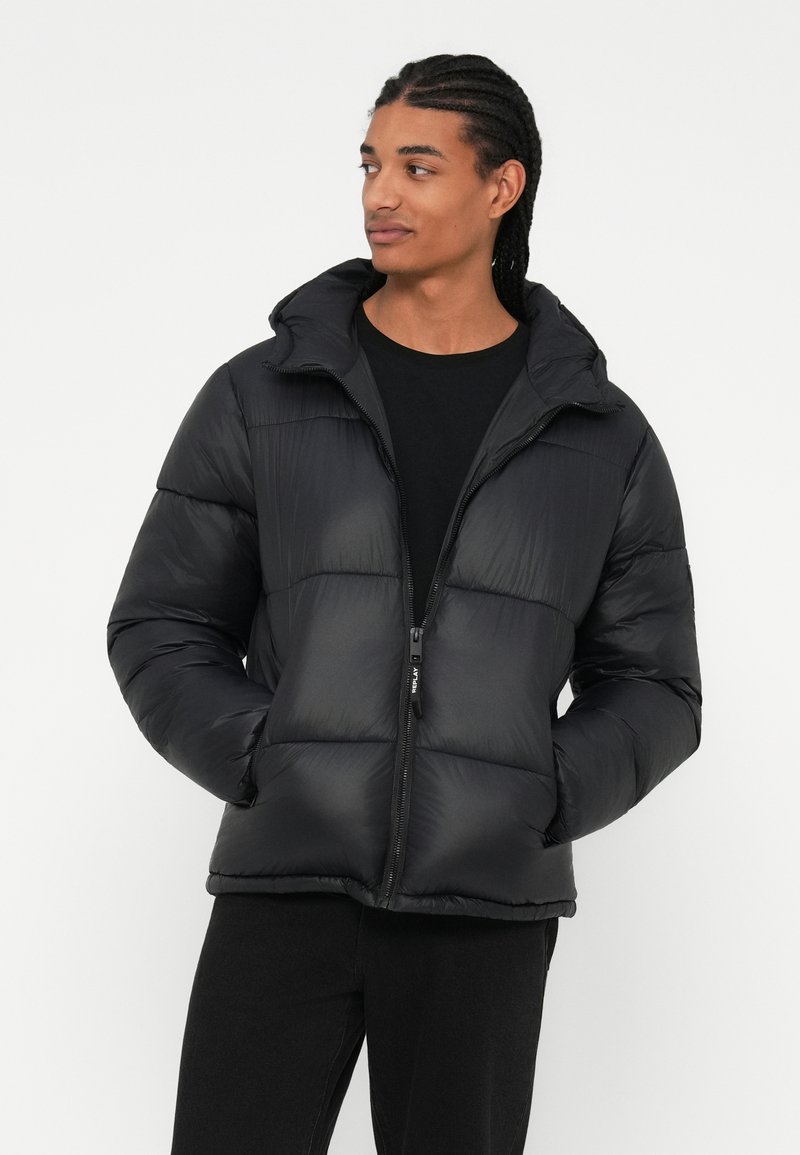 Doudoune noire avec fermeture éclair, capuche et design matelassé. Elle présente une texture lisse avec une coupe slim et des poignets élastiques.