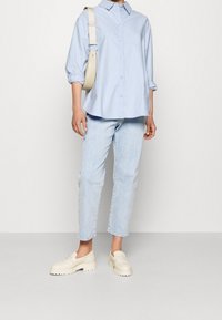 Jasnoniebieska koszula na guziki z podwiniętymi rękawami, w połączeniu z jasnymi dżinsami i kremowymi masywnymi mokasynami. Beżowa torebka na ramię dopełnia stylizację.