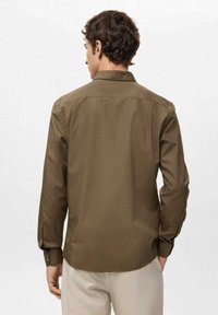 Camisa marrón de manga larga, confeccionada con tela suave, que presenta un cuello, puños abotonados y un diseño recto en la espalda.