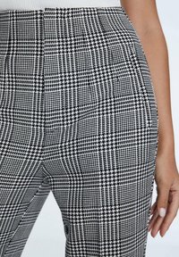Zwart-witte houndstooth-gepatroneerde broeken met een getailleerde pasvorm, voorzien van een plooi aan de voorkant, gemaakt van een glad, textuurstof.