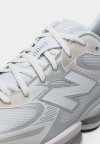 Gros plan d'une basket New Balance 2000 blanche et gris clair avec mesh texturé, lacets et grand logo "N" sur le côté.