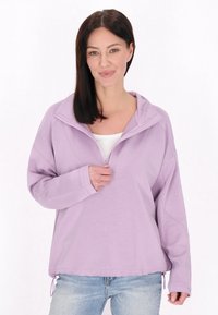 Lyse lilla pullover med halv-zip krave, lange ærmer og en afslappet pasform. Har sidelommelisser og et struktureret materiale.