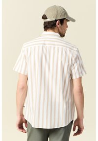 Camisa de manga corta con rayas verticales en beige y blanco, fabricada en suave algodón, con dobladillo curvado y una sola costura en el yugo trasero.