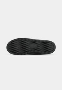 Semelle de chaussure noire avec motif de bande de roulement triangulaire et zone rectangulaire pour le logo au centre sur fond blanc.