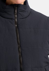Giacca puffer blu scuro con colletto alto, zip frontale e motivo trapuntato orizzontale. Realizzata in un tessuto leggero e testurizzato.