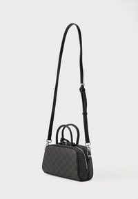 Czarna torebka wykonana z materiału syntetycznego z wzorem monogramu, z podwójnymi uchwytami u góry oraz długim regulowanym paskiem, zamykana na zamek błyskawiczny.