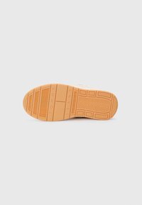 Sole of a sneaker; rubber material in tan with textured grip patterns; features branding "TOMMY JEANS" embossed near the heel.