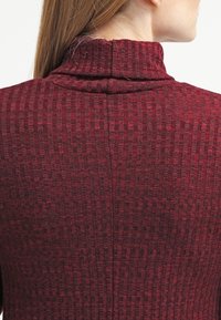 Top in magenta a coste con colletto alto, caratterizzato da un motivo testurizzato e una vestibilità aderente sul retro. Tessuto morbido e elastico.