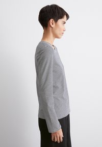 Schwarz-weißer gestreifter Langarmshirt mit rundem Halsausschnitt, ausgestattet mit einer taillierten Passform und weichem Material. Von der Seite gezeigt.