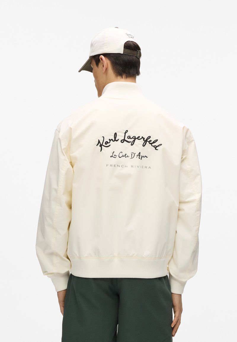 Giacca bomber crema con polsini e orlo a coste, con testo nero ricamato sul retro: "Karl Lagerfeld La Côte D'Azur FRENCH RIVIERA."