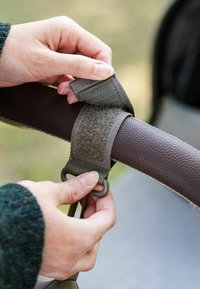 Kädet kiinnittävät harmaan tarranauhan muovikoukuilla ruskean nahkailinohjauksen ympärille ulkona.