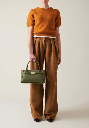 Pull orange à manches courtes, tissu texturé ; pantalon plissé taille haute marron ; sac à main en cuir vert avec quincaillerie dorée ; chaussures noires.