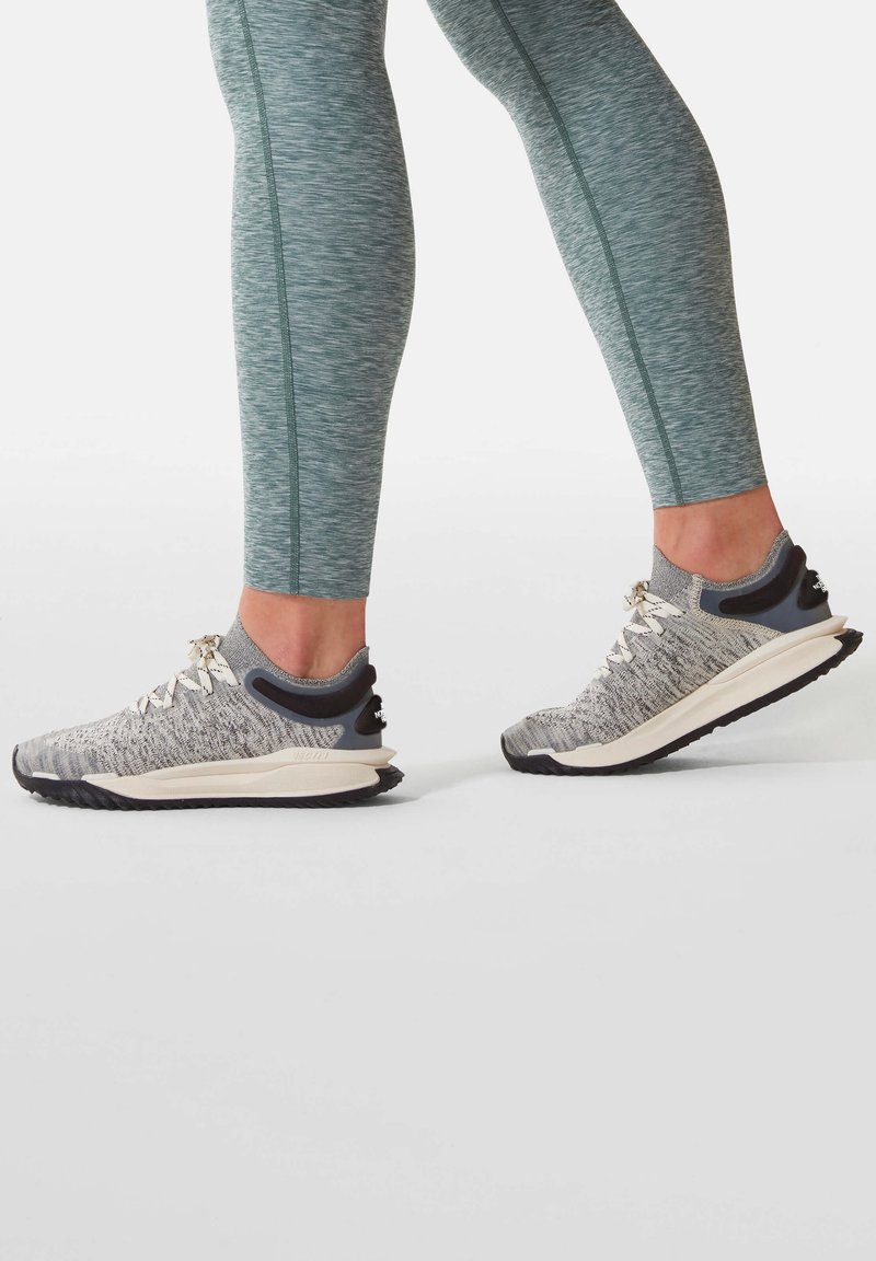 Šedé a bílé sportovní boty s lehkým pleteným svrškem, texturovanou podrážkou a reflexními prvky. Kombinované s tyrkysovými přiléhavými legínami.