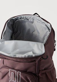 Σακίδιο πλάτης μπορντό με γκρι εσωτερικό, κλείσιμο με φερμουάρ και δίχτυ πλαϊνή τσέπη. Διαθέτει λεία υφή και μινιμαλιστικό σχέδιο.