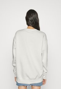 Sudadera gris claro con un corte relajado, mangas largas y un cuello redondo ribeteado. La tela parece suave y texturizada.