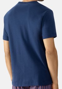 Navyblauwe katoenen T-shirt met korte mouwen, ronde hals en een gladde textuur, weergegeven vanuit de achterkant. Subtiele stikseldetails zijn te zien.