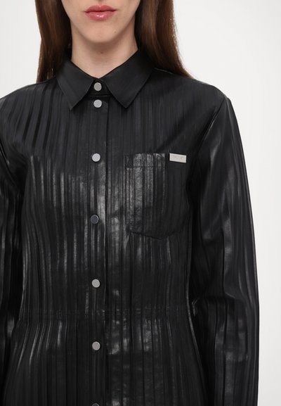 Schwarzes, plissiertes Hemdkleid aus glänzendem Material mit einem spitzen Kragen, silbernen Knöpfen und einer Fronttasche mit einem Markenzeichen.