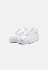Weiße Sneaker mit Obermaterial aus Leder, flachen Schnürsenkeln, gepolsterter Zunge, Gummisohle und dezentem Logo-Detail an der Seite. Abgerundete Zehenpartie und strukturierte Akzente.