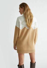 Abito in maglia color beige con parte superiore bianca. Presenta un motivo geometrico e orlo a coste. Maniche lunghe e vestibilità rilassata.