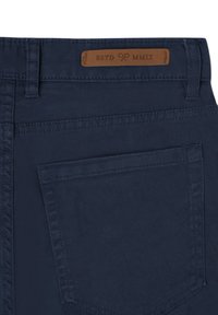 Vaqueros de mezclilla azul marino con un bolsillo trasero, con costuras en contraste y una etiqueta de cuero grabada con "ESTD MMIX" en la cintura.