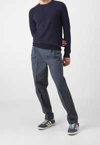 Marinblå stickad tröja, grå veckade byxor och grå sneakers med vita detaljer. Minimalistisk design med texturerad tyg och avslappnad passform.