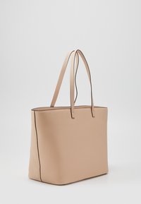 Beige draagtas van gestructureerd materiaal met twee lange schouderbanden en contrasterende stiksels langs de randen. Rechthoekige vorm, minimalistisch ontwerp.
