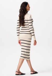 Haken midi-jurk in beige met zwarte horizontale strepen; aansluitend ontwerp, lange mouwen, geribbelde textuur, gecombineerd met zwarte platte schoenen.