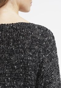 Svart och vit stickad tröja med en lös passform, texturerad tyg och bred halsringning, med synliga sömnads mönster genom hela plagget.