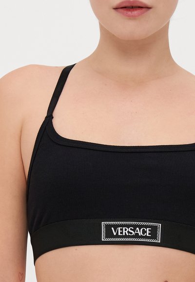 Melna ribota bandeau krūšturis ar plānām siksnām un biezu melnu joslu, kas rotāta ar baltu "VERSACE" logo etiķeti. Gluda tekstūra, pieguļošs dizains.
