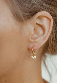Orecchini a cerchio a forma di cuore in oro, con un gruppo decorativo di piccole pietre trasparenti, appesi a un sottile cerchio.